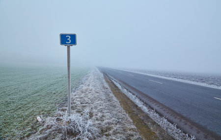 Winter morning. Fog drifts over trees covered in white frost. A good asphalt road leads into the distance and disappears into the fog.の写真素材