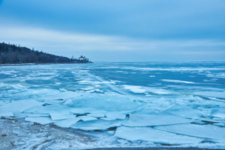 A serene winter scene featuring a pristine, icy-blue lake with a snow-covered shore. The tranquil...