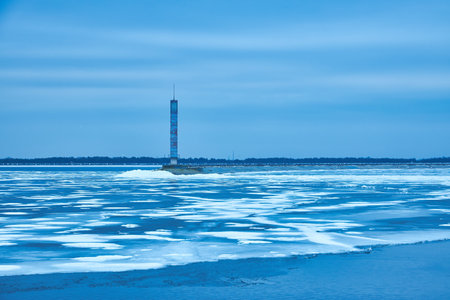 An enchanting winter scene with a tranquil reservoir, vibrant blue ice, and a solitary lighthouse.の写真素材
