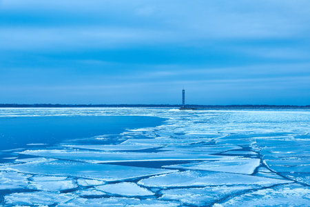An enchanting winter scene with a tranquil reservoir, vibrant blue ice, and a solitary lighthouse.の写真素材