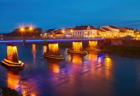Beautiful view of the night city, in the foreground there is a river and a pedestrian bridge, in the river the lights of the night city are displayedの写真素材