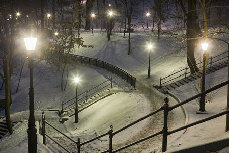 Winter evening in the park, snow-covered benches, bright lights illuminated white snow, New Year's Eve with snow.の写真素材