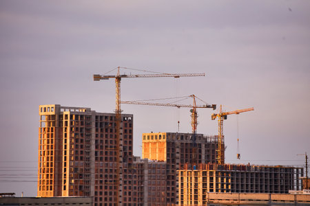 Construction site with cranes and unfinished buildings under warm sunset light. The scene highlights the progress of urban development in a city.の写真素材
