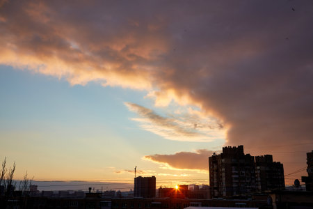 A breathtaking sunset casting warm golden light across the city skyline. The dark clouds contrast with the soft hues of the setting sun, creating a dramatic and serene atmosphere.の写真素材