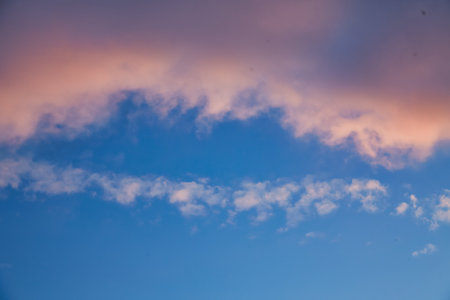 A calm sky with soft golden clouds illuminated by the setting sun. The subtle transition from bright blue to warm orange creates a peaceful and dreamy atmosphere over the horizon.の写真素材