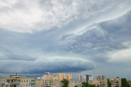 Massive storm clouds gather over a city skyline, creating a dramatic contrast between the dark, swirling sky and the tall buildings below. The scene captures the intensity of an impending storm.の写真素材