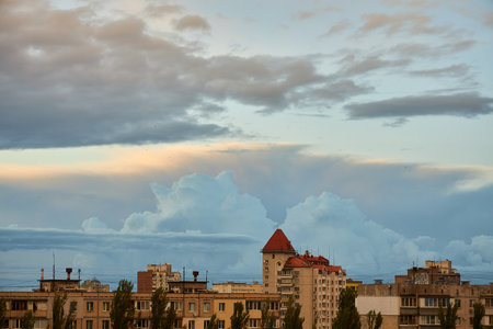 A serene cityscape under a sky filled with towering clouds and soft evening light. The buildings contrast with the dramatic cloud formations, creating a peaceful yet dynamic urban scene.の写真素材