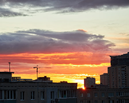 A city skyline at dusk with a gradient sky transitioning from warm orange to deep blue. The silhouettes of buildings and cranes are visible against the glowing horizon.の写真素材