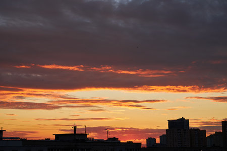 A city skyline at dusk with a gradient sky transitioning from warm orange to deep blue. The silhouettes of buildings and cranes are visible against the glowing horizon.の写真素材