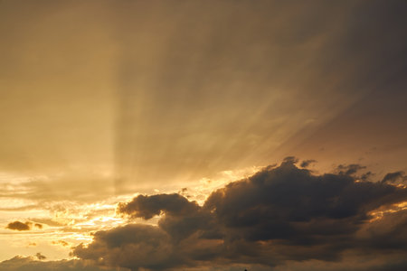 Dramatic sky with sun rays breaking through clouds during dusk, casting a soft light and creating a serene, atmospheric view. The light gradients beautifully highlight the cloud formations.の写真素材
