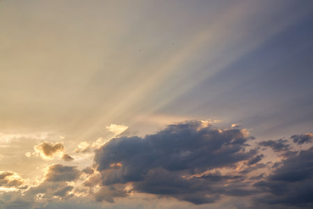 Dramatic sky with sun rays breaking through clouds during dusk, casting a soft light and creating a serene, atmospheric view. The light gradients beautifully highlight the cloud formations.の写真素材