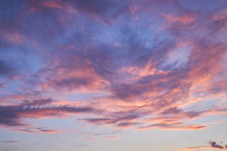 A beautiful sunset sky filled with soft pink, purple, and blue hues. The clouds are illuminated by the setting sun, creating a peaceful and serene atmosphere, ideal for backgrounds and designs.の写真素材