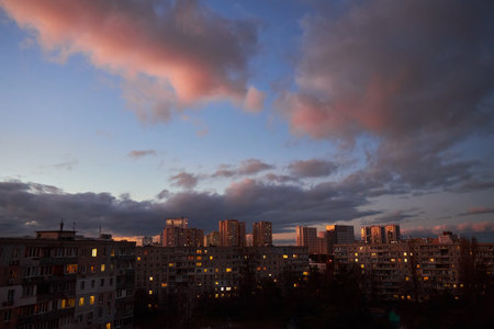 Apartment buildings framed by a dramatic cloudy sky at sunset. Dark clouds and hints of pink on the horizon create a moody, urban atmosphere.の写真素材