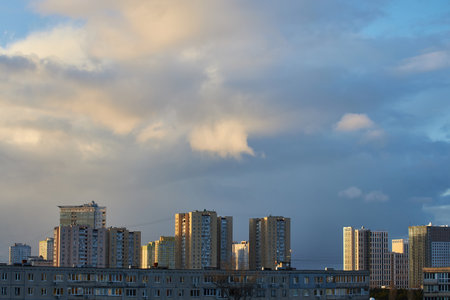 A serene cityscape under a sky filled with towering clouds and soft evening light. The buildings contrast with the dramatic cloud formations, creating a peaceful yet dynamic urban scene.の写真素材