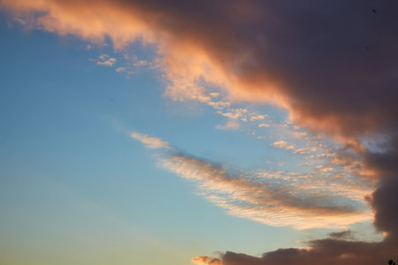 A breathtaking sunset casting warm golden light across the skyline. The dark clouds contrast with the soft hues of the setting sun, creating a dramatic and serene atmosphere.の写真素材