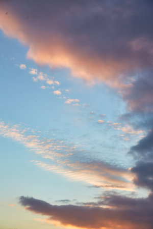 A calm sky with soft golden clouds illuminated by the setting sun. The subtle transition from bright blue to warm orange creates a peaceful and dreamy atmosphere over the horizon.の写真素材