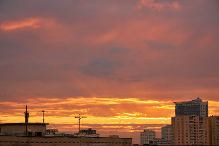 A city skyline at dusk with a gradient sky transitioning from warm orange to deep blue. The silhouettes of buildings and cranes are visible against the glowing horizon.の写真素材