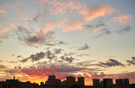 A vibrant sunset with intense orange and yellow hues highlights the silhouettes of buildings and a construction crane, creating a dramatic skyline under a cloudy sky.の写真素材