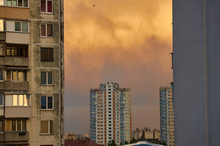 Apartment buildings framed by a dramatic cloudy sky at sunset. Dark clouds and hints of pink on the horizon create a moody, urban atmosphere.の写真素材