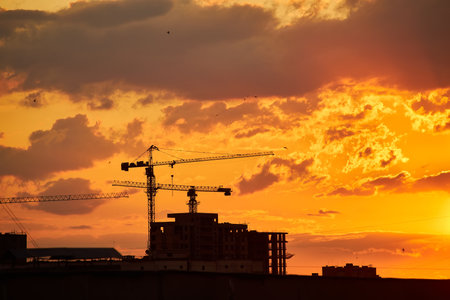 A city skyline at dusk with a gradient sky transitioning from warm orange to deep blue. The silhouettes of buildings and cranes are visible against the glowing horizon.の写真素材