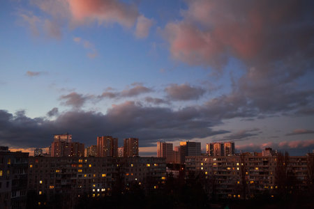 A vibrant sunset sky with dark clouds and orange highlights contrasts against the city skyline. The moody atmosphere captures the beauty of a changing sky over an urban landscape.の写真素材