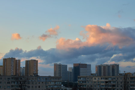 A stunning sunset sky filled with colorful pink, orange, and blue clouds over a distant city skyline. The vibrant hues and soft light create a peaceful and dynamic urban atmosphere.の写真素材