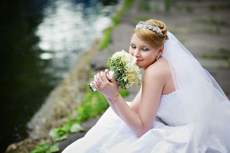 Happy bride in wedding dress near lake with bouquet of flowersの写真素材