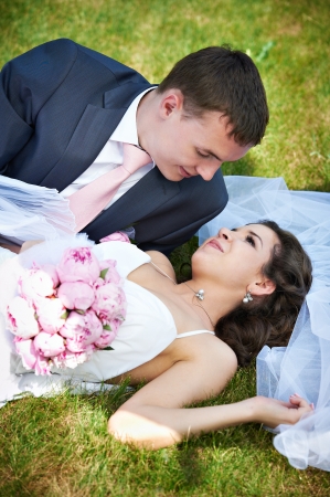 Happy bride and groom lying on grass in parkの写真素材