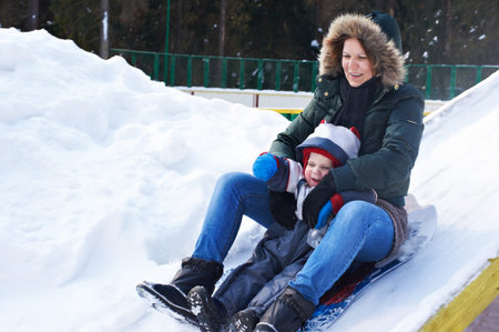 Mother and son sledding down the hill, snow, winter の写真素材