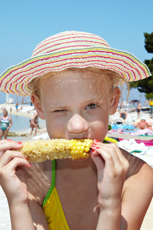 Girl in hat eating corn on a sunny beachの写真素材