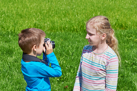 Little boy with retro SLR camera shooting girl outdoorsの写真素材