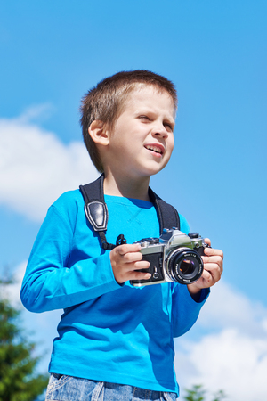 Little boy with retro SLR camera on blue sky looks into the distanceの写真素材