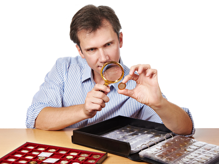 Man numismatist examines with a magnifying glass coin from his collection isolatedの写真素材