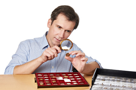 Man numismatist examines with a magnifying glass coin from his collection isolatedの写真素材
