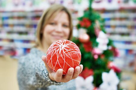 Beauty woman holds red ball for the Christmas tree in the store