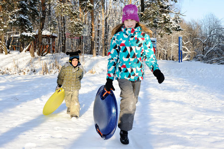 Girl and boy riding with hills on sleds on winter weather