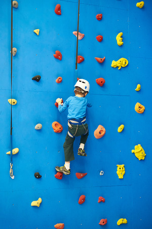 Little boy is climbing to amusement park on blue wallの写真素材