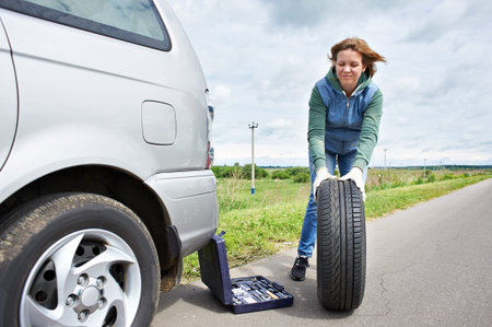 Woman changing a wheel of car on road
