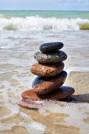 Stones in pyramid and wave on the sand beach