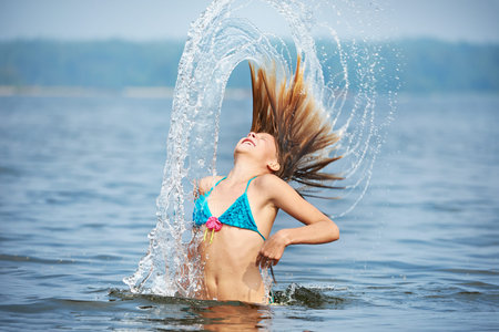 Girl teenager with splashes from hair on the lakeの写真素材