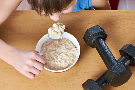 Boy eating porridge and dumbbells as symbols of sports lifestyleの写真素材