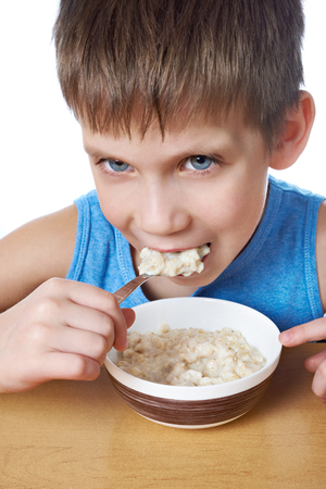Little boy eating porridge at the table isolated whiteの写真素材