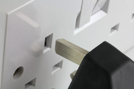 A UK  three pin plug being lined up before connecting to wall plate socket