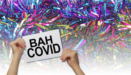 Bah Covid Concept Background â hands holding a white placard with the words BAH COVID against a graduated Christmas tinsel background with copyspaceの写真素材