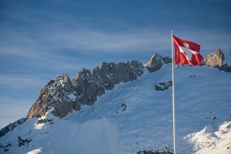 A Swiss flag blowing in the wind in front of the Fusshoerner.の写真素材