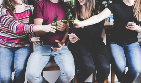 Modern party lifestyle - A group of young millennium people sit in the kitchen on chairs and drink...