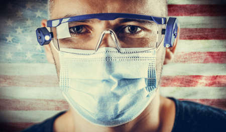 Doctor in protective glasses and a mask against the background of the flag of his country.の写真素材