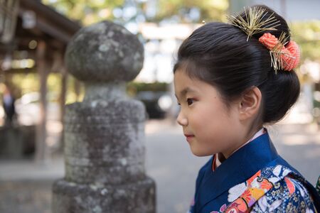 A young Japanese girl in a kimono outdoors at a shrine.の写真素材