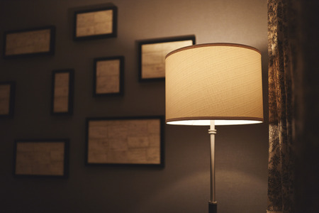 A lamp in a dark corner of a hotel room with abstract frames out of focus on the wall behind it and...