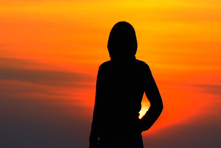 silhouette of the girl in sportswear with a hood at sunsetの写真素材